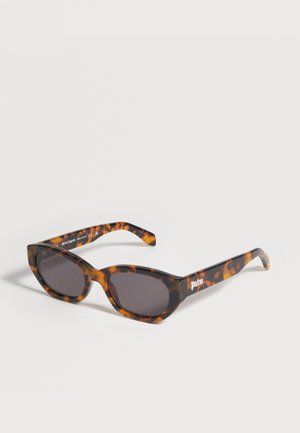 Lunettes de soleil œil de chat à motif écaille de tortue avec verres foncés et logo "palm" sur la branche, posées sur un fond clair uni.