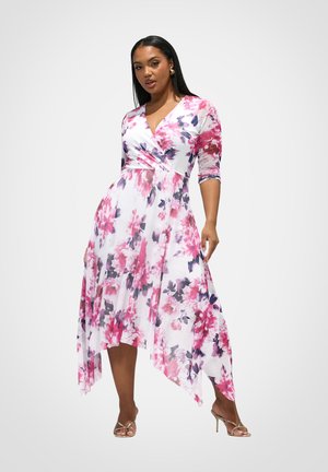 Frau trägt ein rosa-lila geblümtes Wickelkleid mit Zipfelsaum und Dreiviertelärmeln, kombiniert mit goldfarbenen High-Heel-Sandalen.