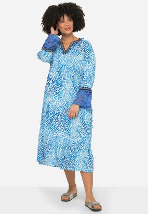 Robe bleue à motifs avec manches longues, présentant un mélange de formes et de lignes. Détails en dentelle aux poignets, décolleté en V et coupe ample.