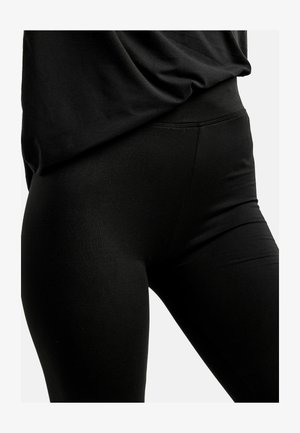 Crne helanke s glatkom teksturom, visokim strukom i dizajnom koji tijesno pristaje uz tijelo. Šavovi naglašavaju oblik, istovremeno zadržavajući minimalistički stil.