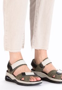 Sandales vert olive avec accents blancs, dotées de sangles réglables, d'une semelle intermédiaire rembourrée et d'une semelle noire texturée, idéales pour un usage décontracté.