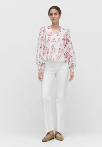 Hvid blomsterbluse med pink detaljer, puffærmer og blondeudsmykning. Kombineret med hvide bukser og brune flade sko for et koordineret look.