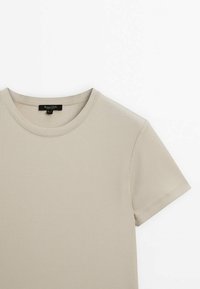 T-shirt beige côtelé à manches courtes avec encolure ronde et étiquette de marque noire visible à l'intérieur du col.