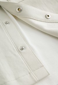 Gros plan sur un tissu beige avec des boutons-pression argentés partiellement ouverts sur un vêtement montrant les détails des coutures et de la texture.