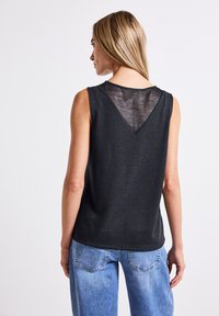 Top senza maniche nero con un pannello in rete testurizzata a forma di V sul retro, abbinato a jeans azzurri chiari. Tessuto morbido con vestibilità rilassata.