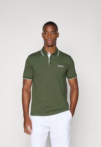 Polo verde oliva con colletto; bottoni bianchi e strisce di accento, con un piccolo logo bianco "BOSS" sul lato sinistro del petto.
