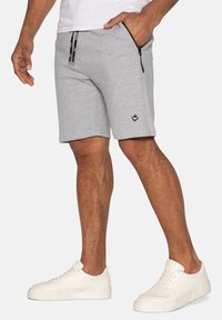 Grå atletiske shorts med en glat tekstur, udstyret med en sort logo-patch, lynlåslommer og en snoreliv. Sammen med hvide sneakers.