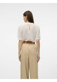 Top blanco de punto texturizado con un detalle de abertura en la espalda, combinado con pantalones beiges de cintura alta. Tejido suave y mangas cortas abullonadas.