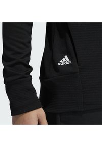 Schwarz Sportlongsleeve-Shirt aus strukturiertem Stoff mit taillierter Passform. Mit weißem Adidas-Logo auf dem Ärmel.