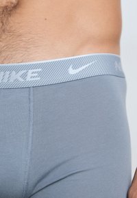 Sive boxer kratke hlače iz mehke tkanine z prugastim svetlo sivim pasom, na katerem je bel Nike logo.