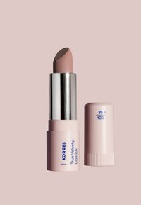 Korres True Velvety Lipstick i en ljusrosa tub med silverdetaljer. Läppstiftet är en mjuk, dämpad rosa färg som visar upp en jämn textur.