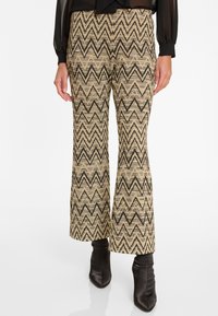 Pantalons évasés beiges avec un motif zigzag noir, en tissu texturé. Assortis à des bottines noires à bout pointu.