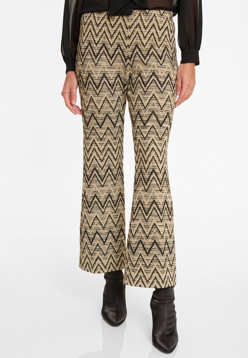 Pantalons évasés beiges avec un motif zigzag noir, en tissu texturé. Assortis à des bottines noires à bout pointu.