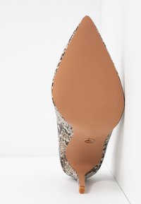 Chaussure à talon haut à bout pointu avec semelle beige et dessus en motif peau de serpent, photographiée par le dessous sur fond blanc.