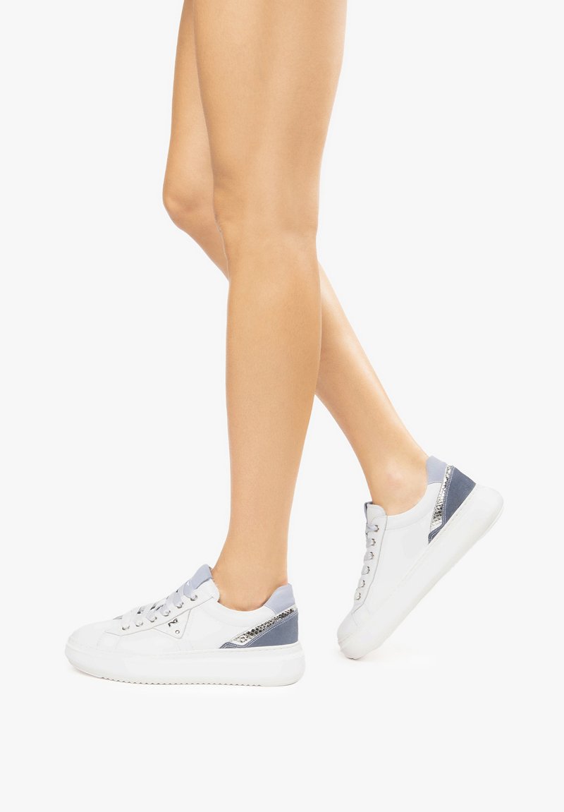 Les chaussures présentent un cuir blanc avec des accents gris, un panneau latéral texturé, une pointe ronde et une semelle épaisse. Les lacets sont de couleur argentée.