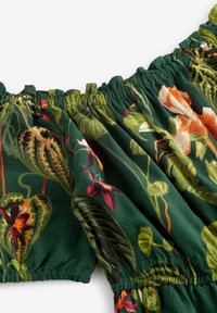 Tissu vert foncé avec bords élastiques froncés et imprimé floral présentant des feuilles et fleurs orange, rouges et de diverses nuances de vert.