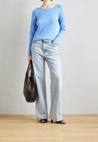 Jasnoniebieska koszula z długim rękawem, luźny krój; spodnie z wysokim stanem, szerokie nogawki w jasnym odcieniu denimu. Niesie dużą czarną skórzaną torebkę, ma na sobie czarne, końcówki spiczaste buty.