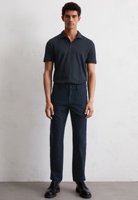Marineblauwe polo met kraag, gecombineerd met donkere broek. De outfit heeft een slim fit en wordt aangevuld met zwarte veterschoenen.