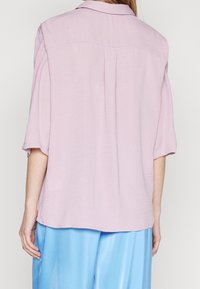 Person wearing a loose light pink short-sleeve shirt and light blue satin pants, shown from the back against a plain background.