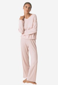 Lichtroze lounge-outfit bestaande uit een relax-fit, geribbelde lange mouw top en wijde broek, beide gemaakt van zachte, gestructureerde stof.