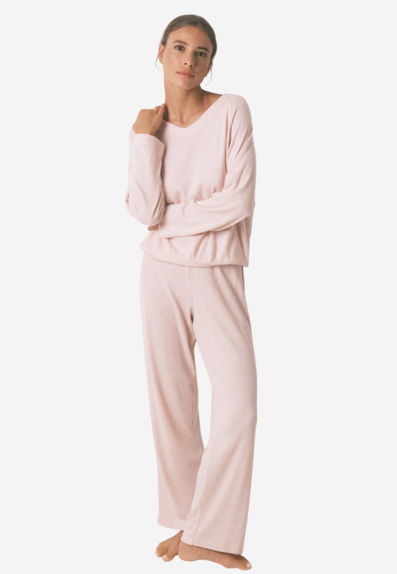 Lichtroze lounge-outfit bestaande uit een relax-fit, geribbelde lange mouw top en wijde broek, beide gemaakt van zachte, gestructureerde stof.
