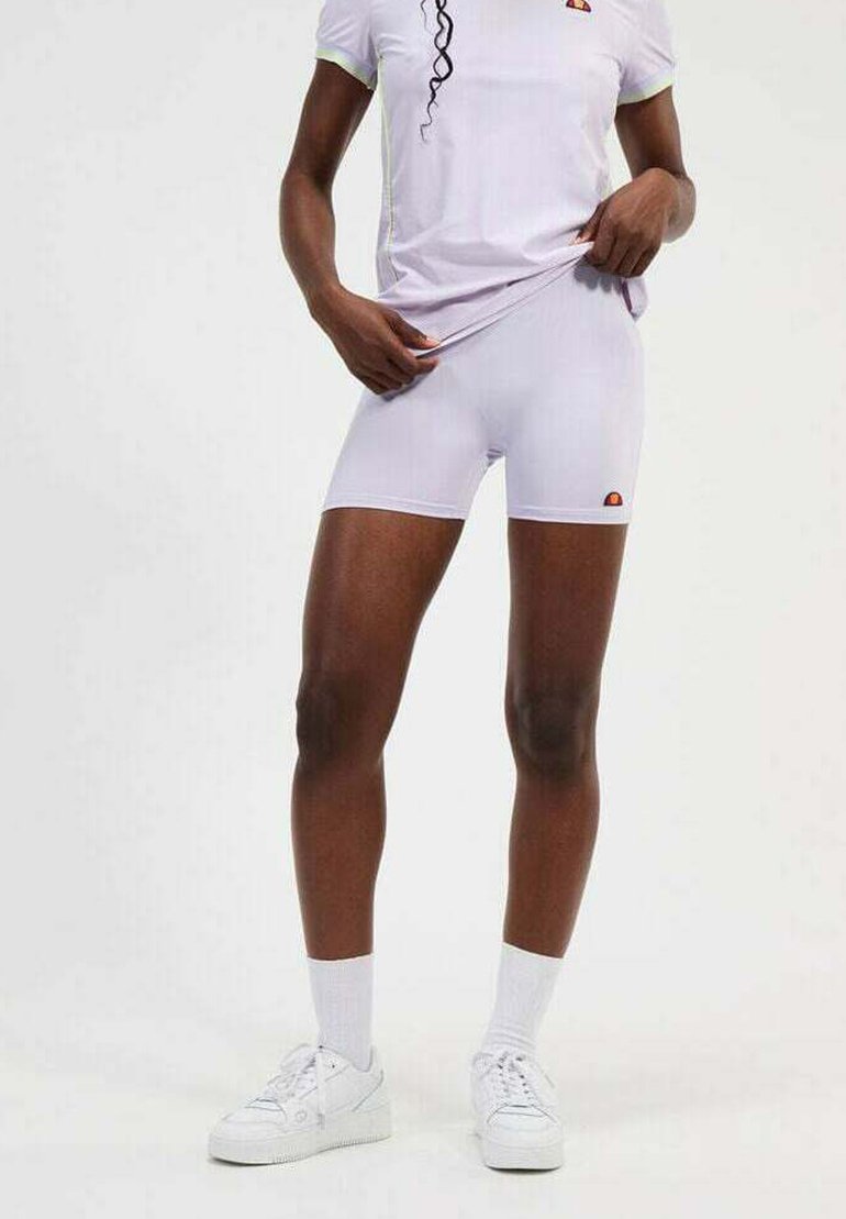 Shorts de sport blancs en matériau léger, avec un petit logo. Portés avec un t-shirt blanc assorti et des baskets blanches avec des chaussettes.