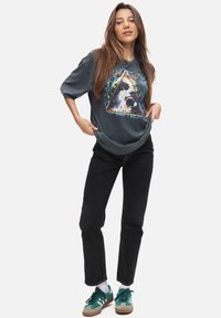 Mörkgrå oversized t-shirt med en färgglad grafik av en hunds ansikte, ihop med svarta jeans och gröna sneakers med bruna detaljer.