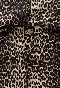 Gros plan d’un tissu imprimé léopard marron, noir et beige avec des boutons noirs et une taille élastique comportant un patch noir avec un logo "ea" stylisé marron.