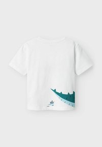 Camiseta blanca de manga corta con un gráfico de cocodrilo en color teal en la parte posterior, con escamas y ojos estilizados, fabricada con material de algodón suave.