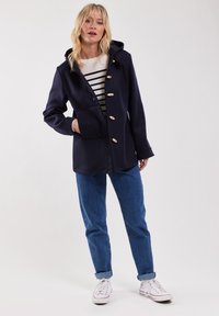 Marinblå kapuschongjacka med stora träknappar, med en enda ficka, som bärs över en randig skjorta och matchas med blåjeans.