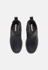Botas de cuero negro hasta el tobillo con una textura suave, cierre de cremallera en ambos lados y un collar acolchado para mayor comodidad. Logo de Timberland visible en el interior.
