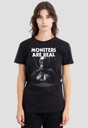 Black cotton t-shirt featuring a graphic print of a monster with the text "MONSTERS ARE REAL" in bold white letters. Short sleeves.