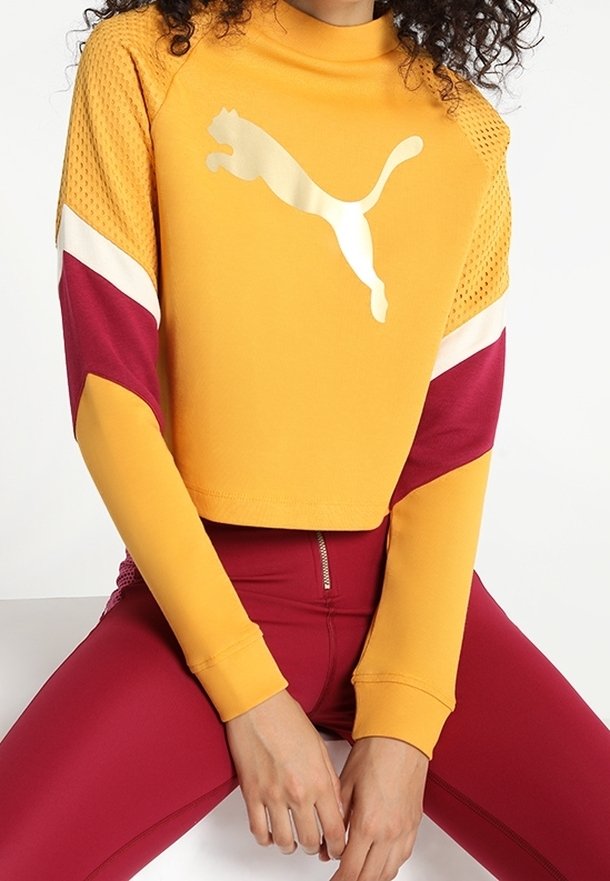 Krótka bluza Puma w intensywnym żółtym kolorze z siateczkowymi detalami, z maroonowymi rękawami akcentującymi oraz odblaskowym logo. Gładka tekstura.
