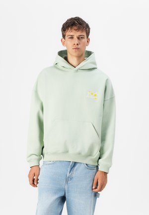 Lichtgroene hoodie van zachte stof, met een voorzak en geborduurde details van gele bloemen boven het linker borstgebied.