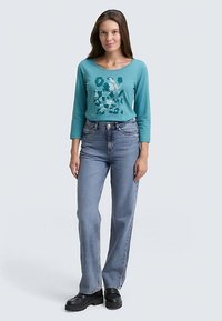 Turquoise long-sleeve shirt with abstract print, paired with high-waisted light blue jeans and black platform shoes. Simple design, casual fit.