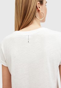 Hvit avslappet t-skjorte med rullet ermer. Har en subtil merkeetikett trykt bak, myk tekstur og en uformell design.