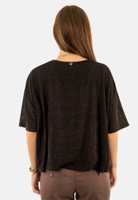 Camiseta negra de corte holgado con mangas cortas, que presenta una textura moteada y un pequeño emblema de corazón en la parte posterior del cuello.