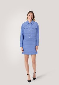 Lichtblauwe tweed korte jas met twee borstzakken, knoopsluiting en bijpassende rok. Beschikt over een textuurpatroon en een gladde stof.