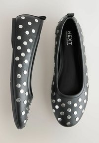 Black leather flats featuring large silver metallic studs evenly spaced across the upper. Rounded toes and a low, flexible sole.