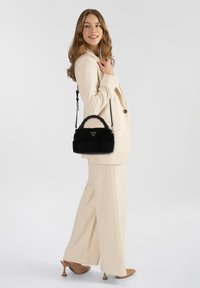 Borsa nera con texture, manico intrecciato, di piccole dimensioni, decorata con un logo, abbinata a un completo color crema e tacchi beige.