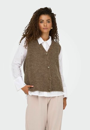 Bruine gebreide vest met V-hals, vijf knopen aan de voorkant, gedragen over een wit shirt. Model toont een ontspannen pasvorm en gestructureerde stof.