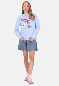 Sudadera azul claro con texto y gráficos de perros, combinada con una falda vaquera. La modelo lleva zapatillas rosas y calcetines blancos.
