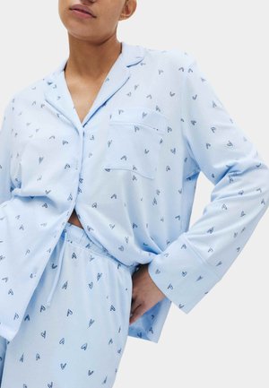 Persona che indossa un pigiama azzurro chiaro con piccoli cuori scuri, composto da una camicia abbottonata con tasca e pantaloni con vita elastica abbinati.