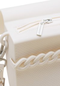 Borsa bianca testurizzata con chiusura a zip e dettaglio in catena. Presenta superfici lisce e una forma rettangolare. Dettaglio della zip visibile.