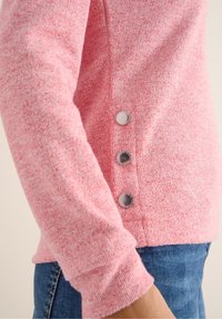 Suéter de punto rosa con tejido texturizado, que presenta tres botones metálicos a lo largo de la costura lateral y un puño acanalado en la muñeca.