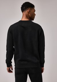 Sort sweatshirts med rund halsudsk�æring, lange ærmer og en struktureret overflade. Har et lille kvadratisk mærke bagpå.