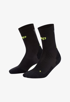 Schwarze Sportstrümpfe mit strukturiertem Design, gerippten Bündchen und reflektierenden Akzenten. Mit gelbem Logo an den Seiten und verstärkten Zehenbereichen.