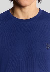 Marineblå bomulls-t-skjorte med rund hals og korte ermer, med en liten brodert logo på venstre bryst. Glatt tekstur.