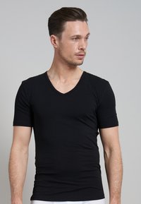 T-shirt noir à manches courtes et col en V, fabriqué en tissu doux, au design ajusté avec une texture lisse et des lignes simples et épurées ; sans motifs visibles.