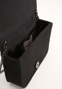 Borsa a tracolla nera in tessuto con chiusura a scatto, dotata di interno foderato e due scomparti. Include una tracolla a catena.